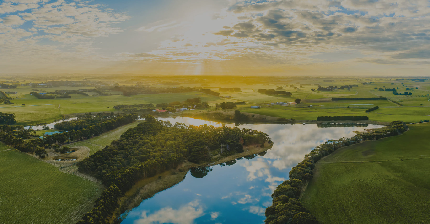 Sun shining down on a green field and river.
